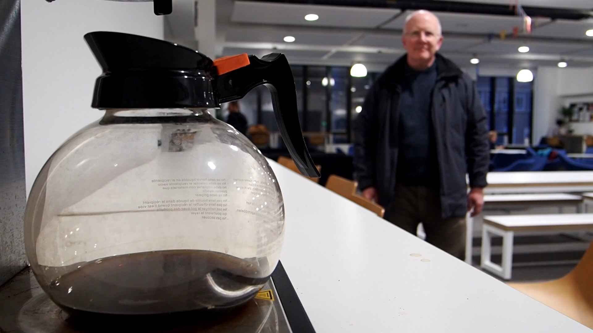 Quentin in the background, with a coffee pot in the foreground. They are inside the original Arup building, at the University of Cambridge.